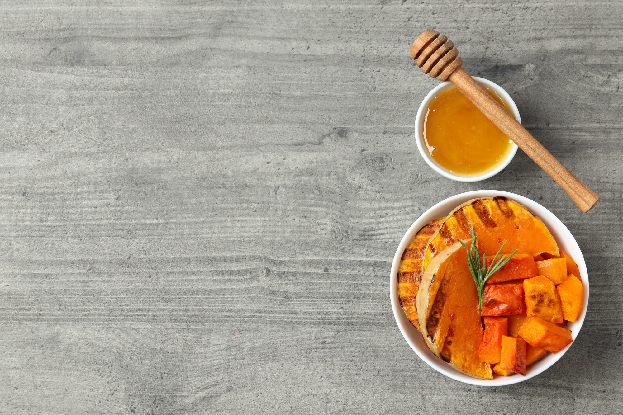 Baked pumpkin, honey and dipper on gray textured background