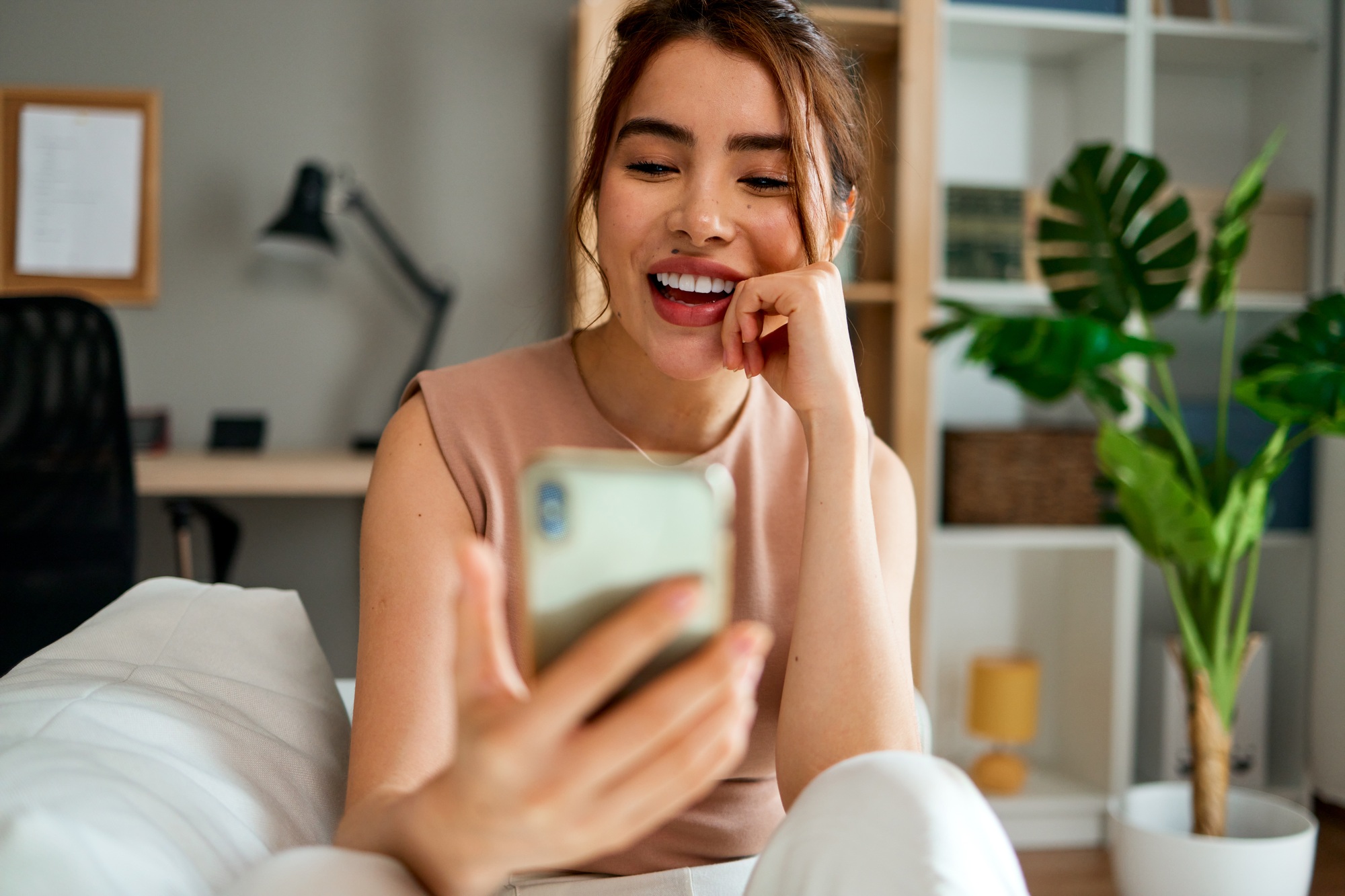 Happy young woman using smartphone at home sitting on sofa in living room